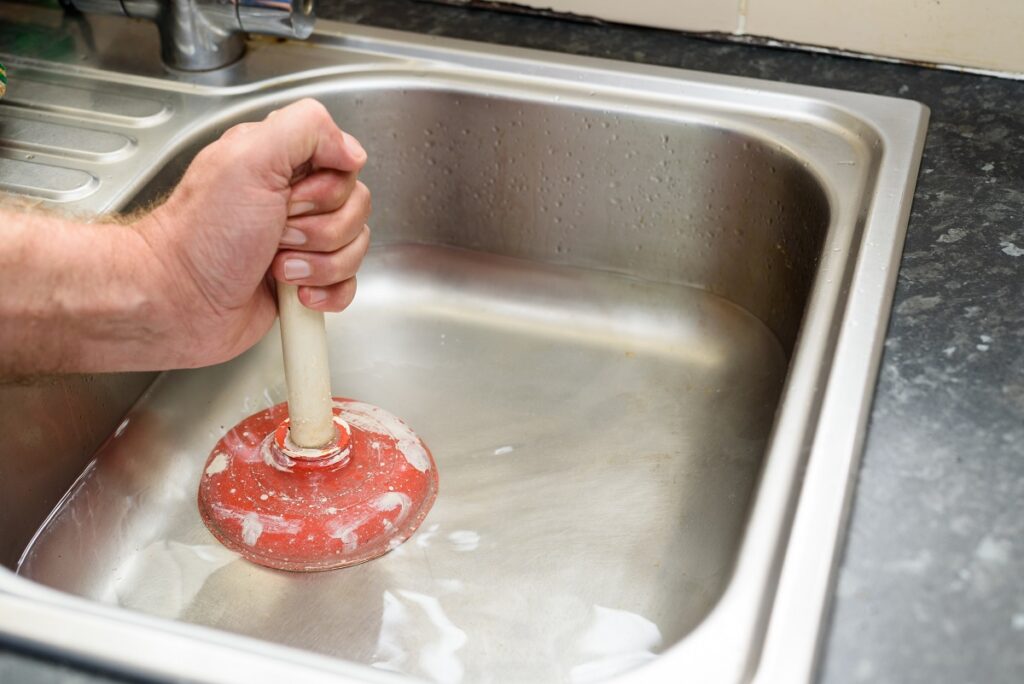 Man holding a plunger and water in sink, used to clean a clogged - Plumber Sydney